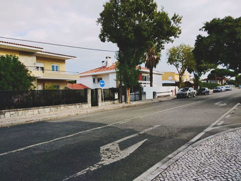 Road by houses and buildings against sky