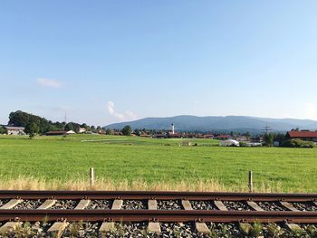 Railroad tracks by green field against sky