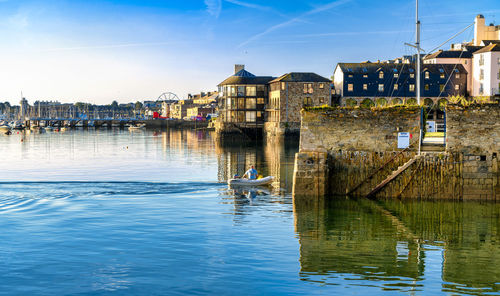 Buildings by river against sky in city