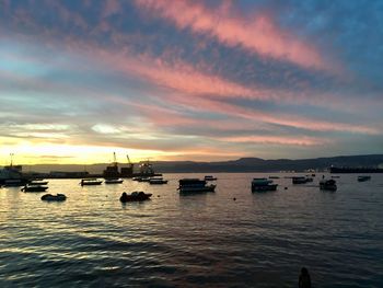 Sailboats moored in sea against sky during sunset