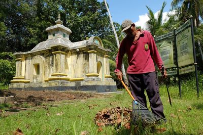 Man cleaning fallen leaves against historic building at park
