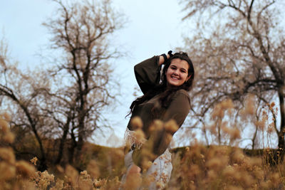 Cheerful young woman posing on field during autumn
