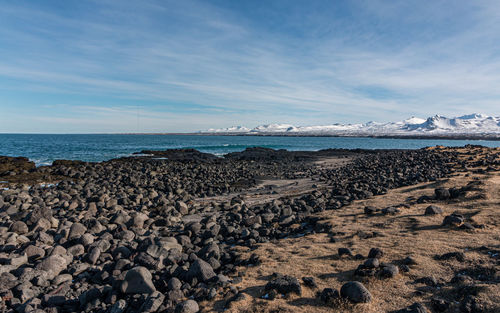 Panoramic view of coastline with volcanic rocks and snow covered mountains in background