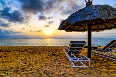 Deck chairs on beach against sky during sunset