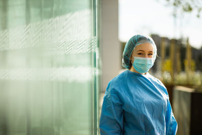 Portrait of young woman standing against window