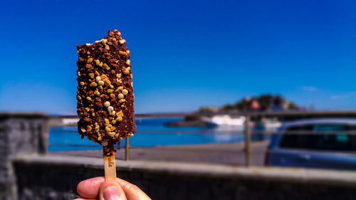 Cropped image of hand holding chocolate ice cream against clear blue sky