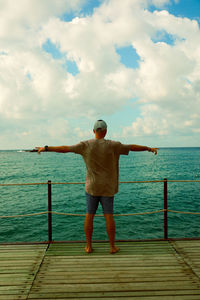 Rear view of man standing on pier over sea against sky