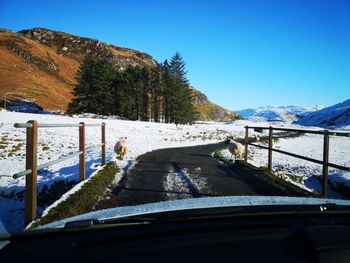 Road by snowcapped mountains against sky seen through car windshield