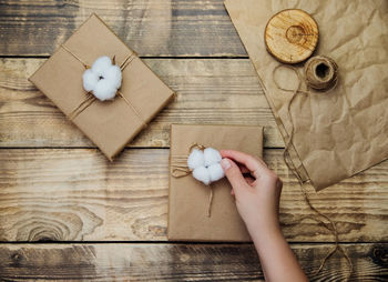 Women's hands hold a box on a wooden background.the decor is made of cotton flowers.