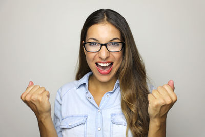 Close-up portrait of cheerful young woman wearing eyeglasses against gray background