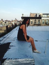 Portrait of woman sitting on retaining wall against sky