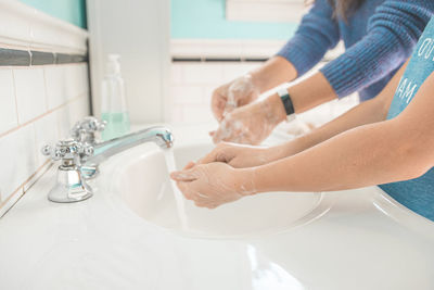 Midsection of women washing hands in sink