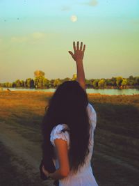 Rear view of woman standing on field against sky during sunset