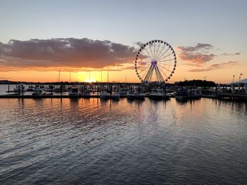 Ferris wheel by sea against sky during sunset