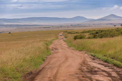 Dirt road amidst landscape against sky