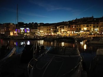 Boats moored at illuminated city against sky at night