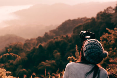 Rear view of woman photographing against sky during sunset