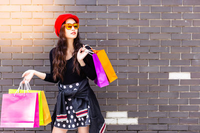 Portrait of young woman holding sunglasses against brick wall