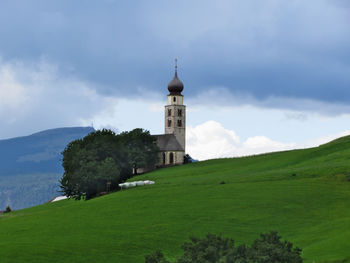 San valentino church by grassy field against cloudy sky