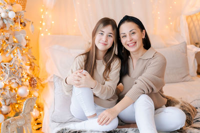 Happy mom and daughter cuddle on bed in decorated bedroom on christmas eve
