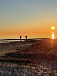 Silhouette people on beach against sky during sunset