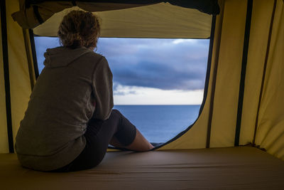 Rear view of woman looking at sea while sitting in tent