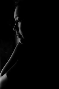 Side view of young woman looking away against black background