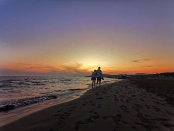 Rear view of men on beach against sky during sunset