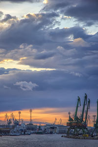 Cranes at commercial dock against sky during sunset