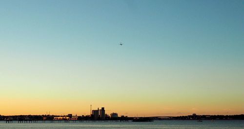 Silhouette airplane flying over sea against clear sky during sunset