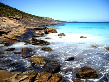 Rocks in sea against clear blue sky