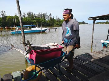 Fisherman carrying dead fish in wheelbarrow on pier over lake 