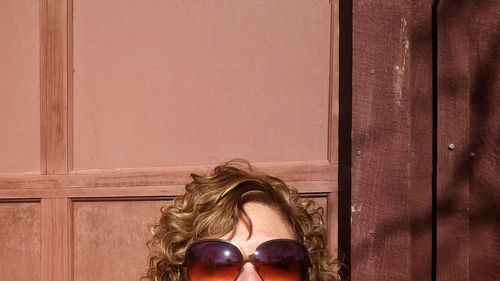 Cropped image of woman wearing sunglass against wooden wall