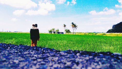 Rear view of woman standing on field against sky