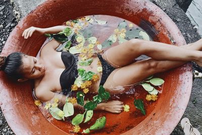 High angle view of woman wearing bikini while lying in container with water and leaves