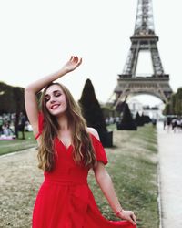 Smiling young woman with eyes closed standing against eiffel tower in park