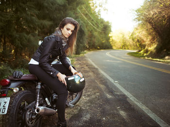 Beautiful woman sitting with helmet on motorcycle at roadside