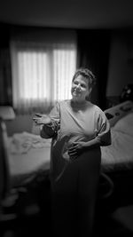 Senior female patient standing with hand on abdomen in hospital ward