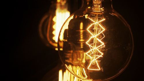 Close-up of illuminated light bulb against black background