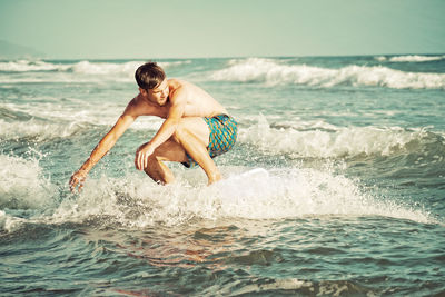 Shirtless man surfing in sea