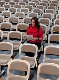 Full length of woman sitting in empty chairs