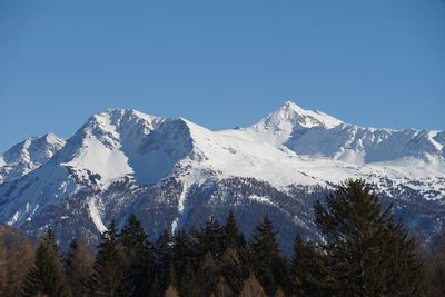 Low angle view of snowcapped mountains against clear blue sky