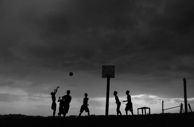 Silhouette boys playing basketball against sky