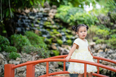 Cute little girl on red bridge in garden.