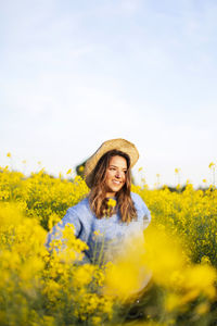 Portrait of smiling young woman with yellow flowers in field against sky