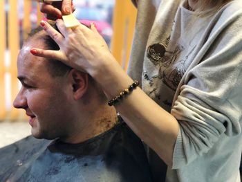 Midsection of man receiving haircut from hairdresser in salon