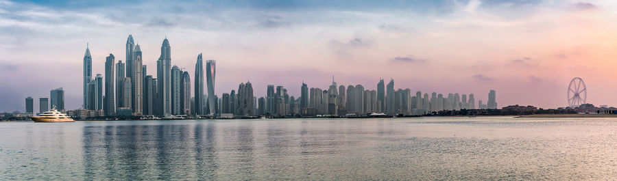 View of city at waterfront against cloudy sky