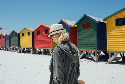 Woman walking by colorful beach huts on sunny day