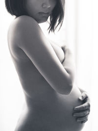 Side view of naked pregnant woman standing at home