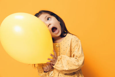 Portrait of young woman with balloons against yellow background